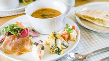 A plate of food with a bowl of soup, a slice of bread, and a salad.
