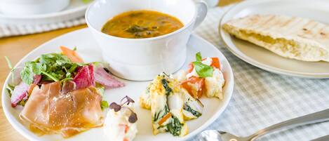 A plate of food with a bowl of soup, a slice of bread, and a salad.