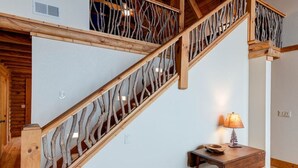 Un escalier en bois doté d’une rampe au design original, une petite table avec une lampe et un mur de couleur claire.