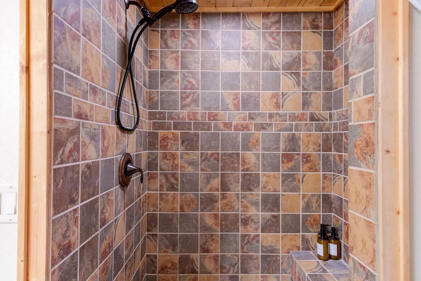 Een douchegedeelte met een betegelde wand en een handdouche.