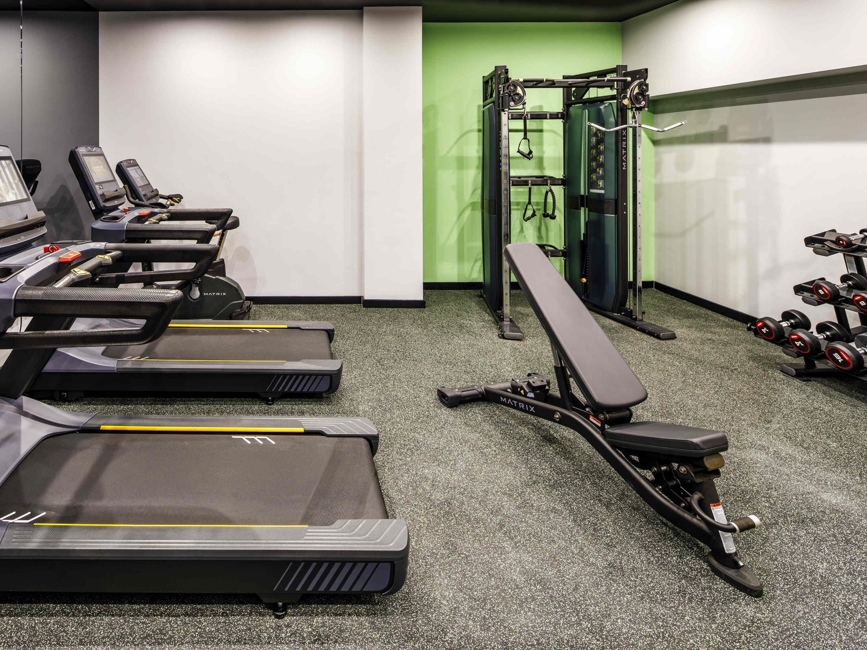 Un gimnasio con cintas de correr, una prensa de banca y mancuernas.