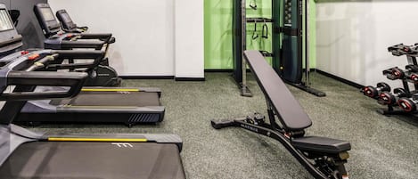 Un gimnasio con cintas de correr, una prensa de banca y mancuernas.