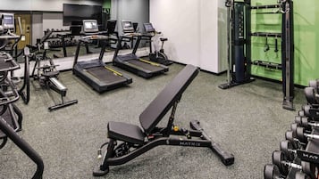 Un gimnasio con cintas de correr, una banca y equipo de levantamiento de pesas.