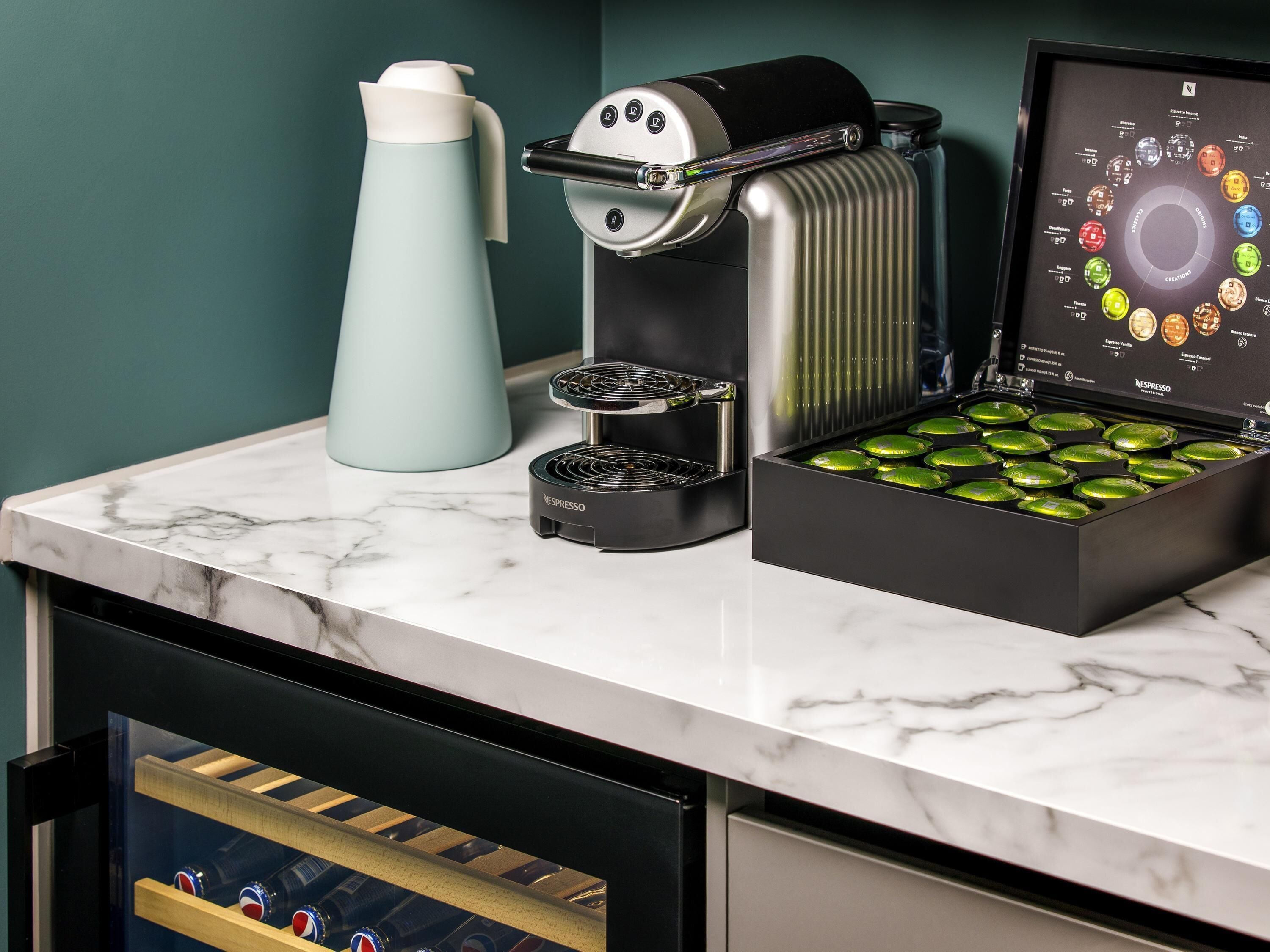 A kitchen with a coffee machine, a kettle, and a box of coffee pods.