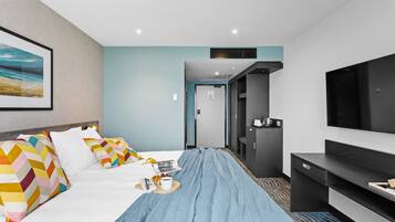 Una habitación de hotel con cama, televisión, escritorio y puerta que da a un baño.