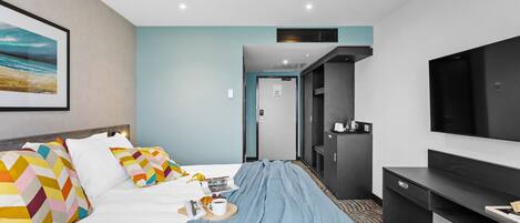 A hotel room with a bed, a TV, a desk, and a door leading to a bathroom.