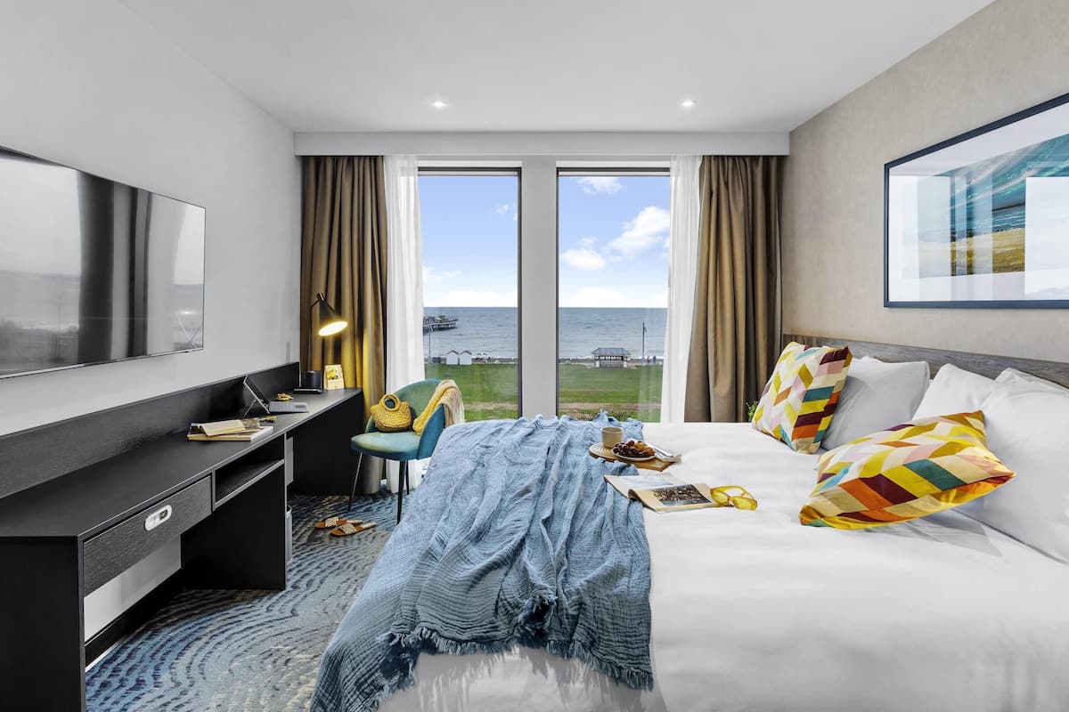 Habitación de hotel con cama, escritorio, televisión y vista al mar.