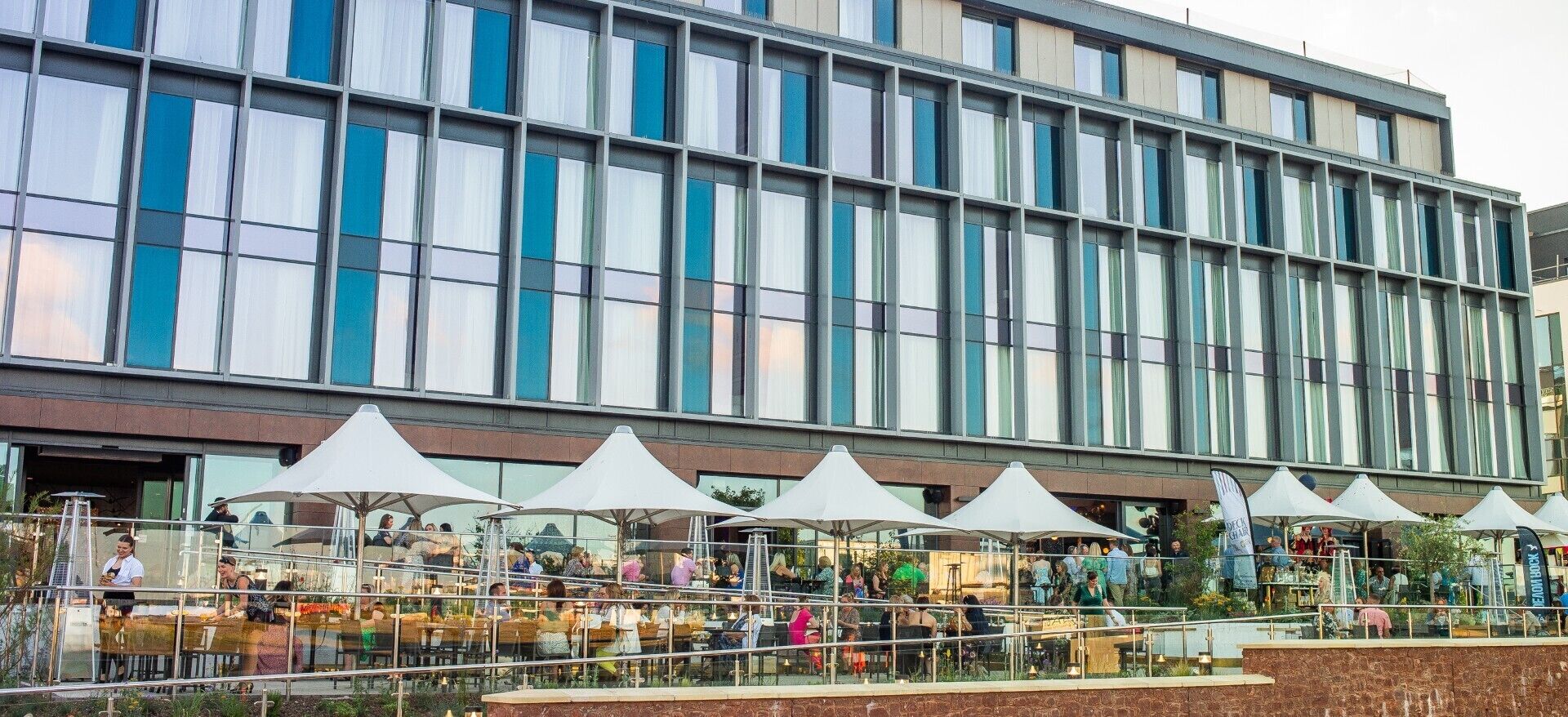 A modern building with a glass facade and outdoor seating area with umbrellas.