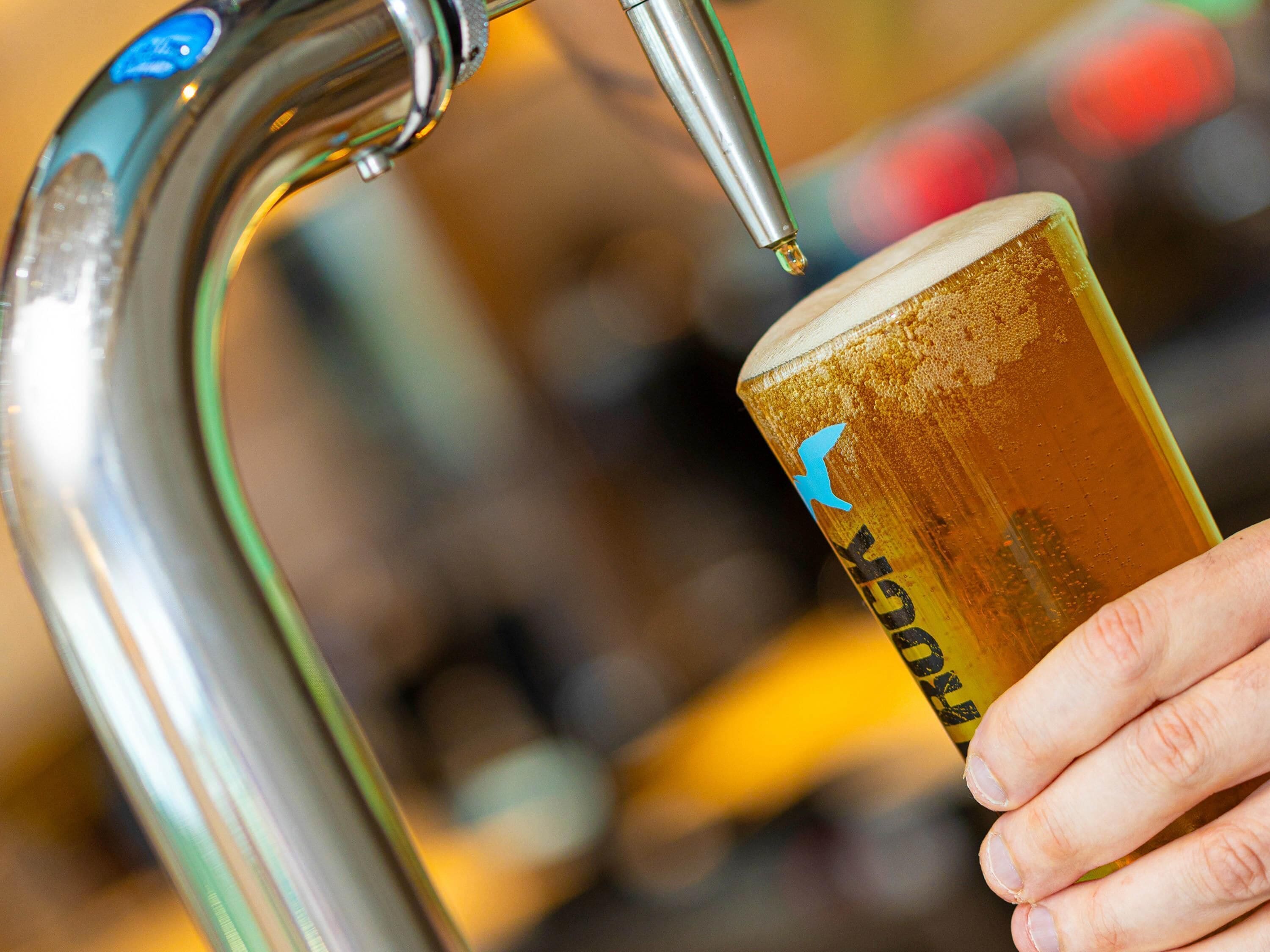 Une main tenant un verre orné d’un logo, sous un robinet.