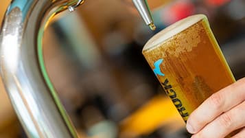 A hand holding a glass with a logo, under a faucet.