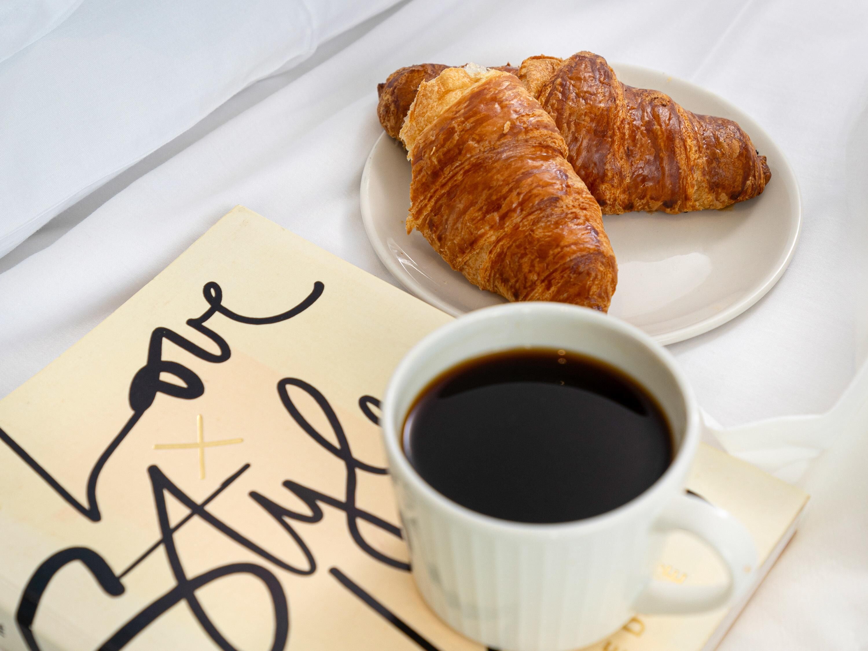 Une table dressée pour le petit-déjeuner avec des croissants, une tasse de café et une serviette sur laquelle est écrit un message.