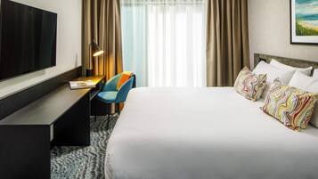 A hotel room with a large bed, a desk, a chair, a TV, and a window with curtains.