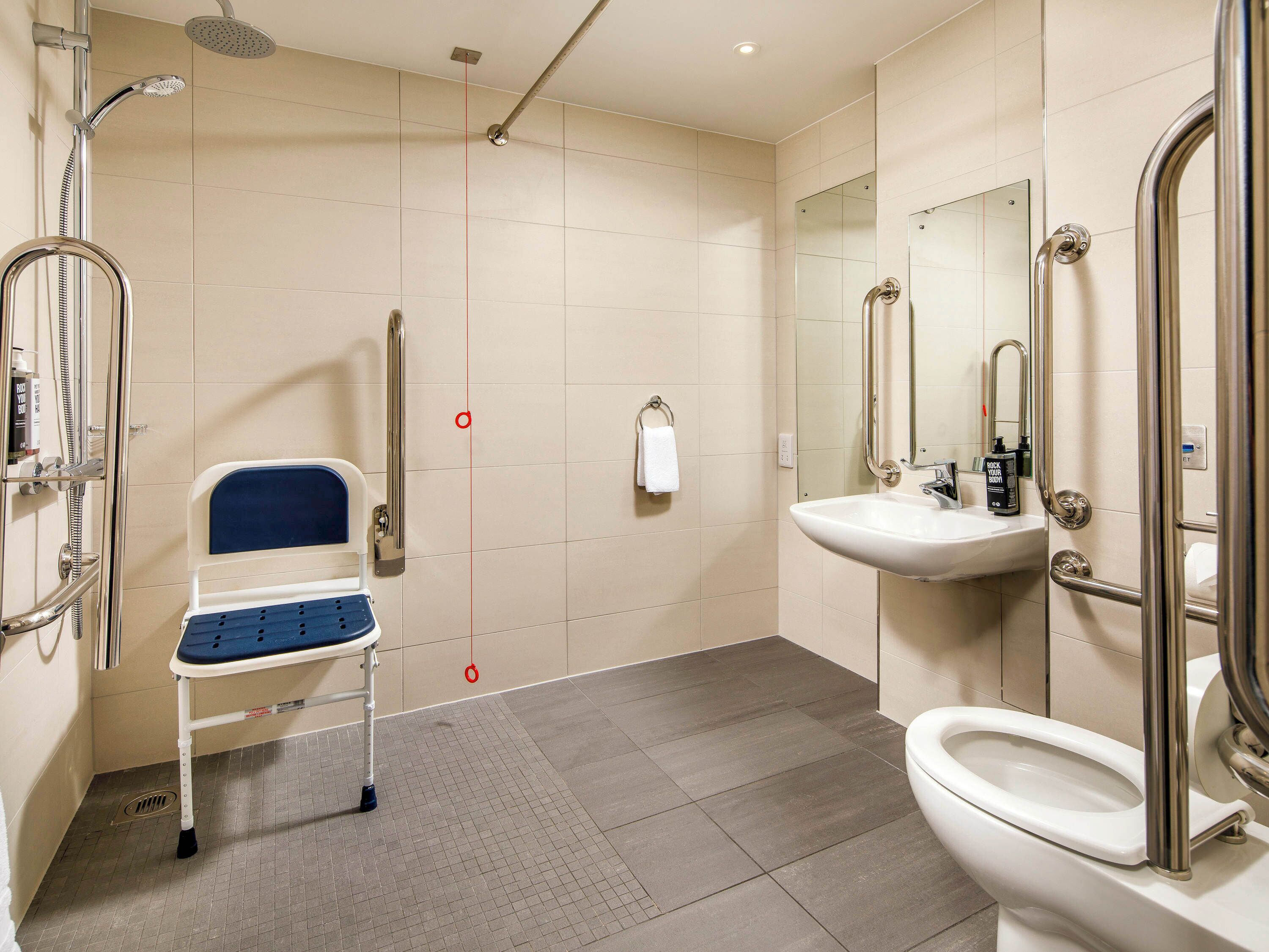 Ein modernes Badezimmer mit Dusche, Toilette, Waschbecken und einer rollstuhlgerechten Sitzbank.