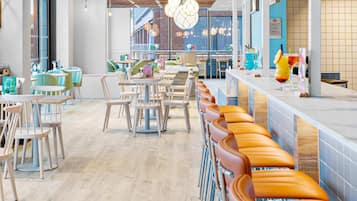 A modern cafe with wooden ceiling panels, a long counter with orange cushioned seating, and a view of the city through large windows.