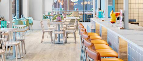A modern cafe with wooden ceiling panels, a long counter with orange cushioned seating, and a view of the city through large windows.