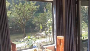 Una habitación con cama, una mesa con sillas, cafetera y vista a un jardín por la ventana.