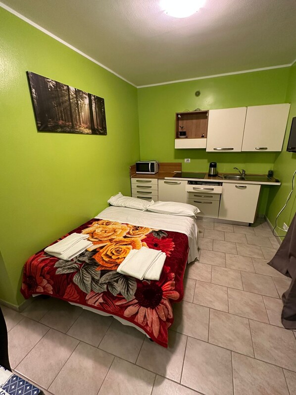 Una habitación pequeña y luminosa con una cama, kitchenette y una pared verde.