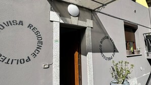 A building with a grey facade and a yellow upper section, featuring a circular sign with "POLICE RESIDENCE" and a door leading into the building. - Residence Politecnico Bovisa (Milan)