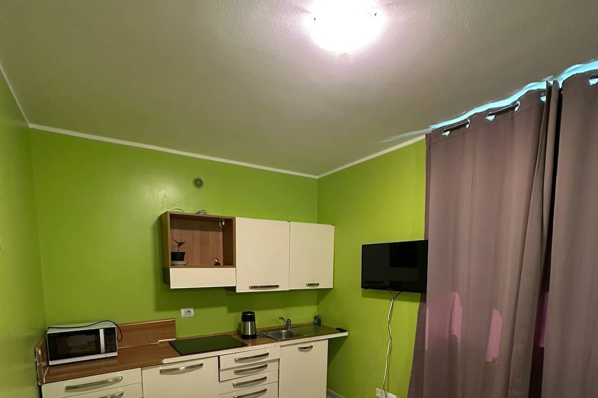 Quarto de hotel compacto com cozinha compacta, cama com colcha florida e televisão fixada na parede.