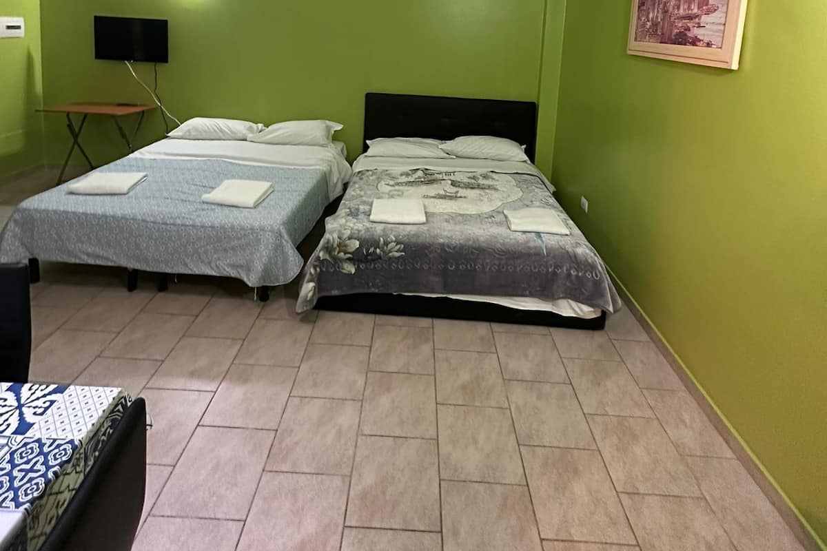 Quarto com duas camas, televisão de tela plana, quadro na parede e uma mesinha com abajur.