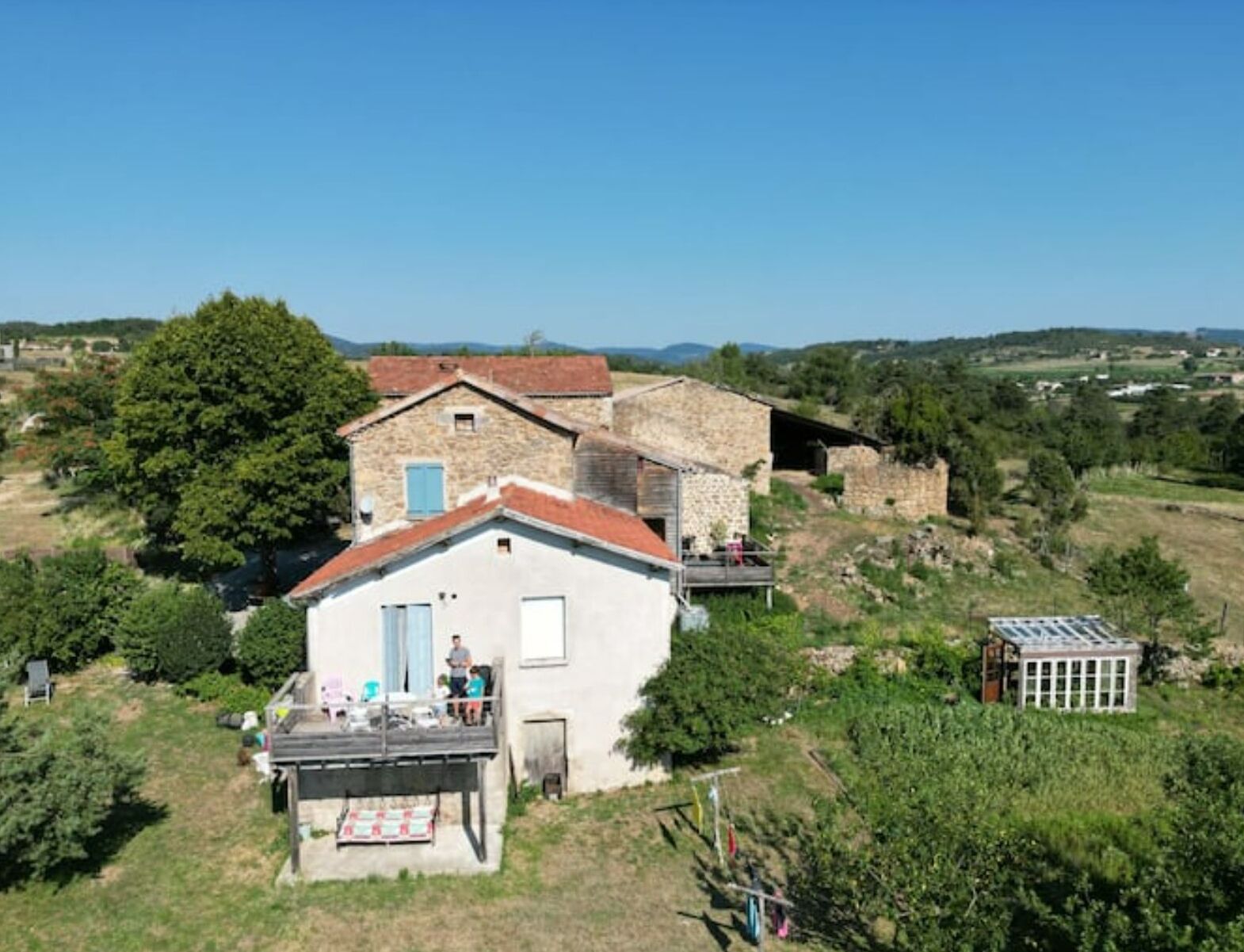 A rustic stone house with a red-tiled roof, a balcony, and a small attached structure.