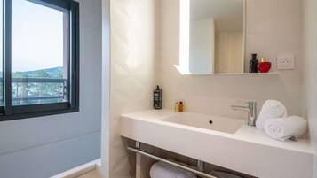 A modern bathroom with a large window, a white sink, a mirror, and a towel rack.