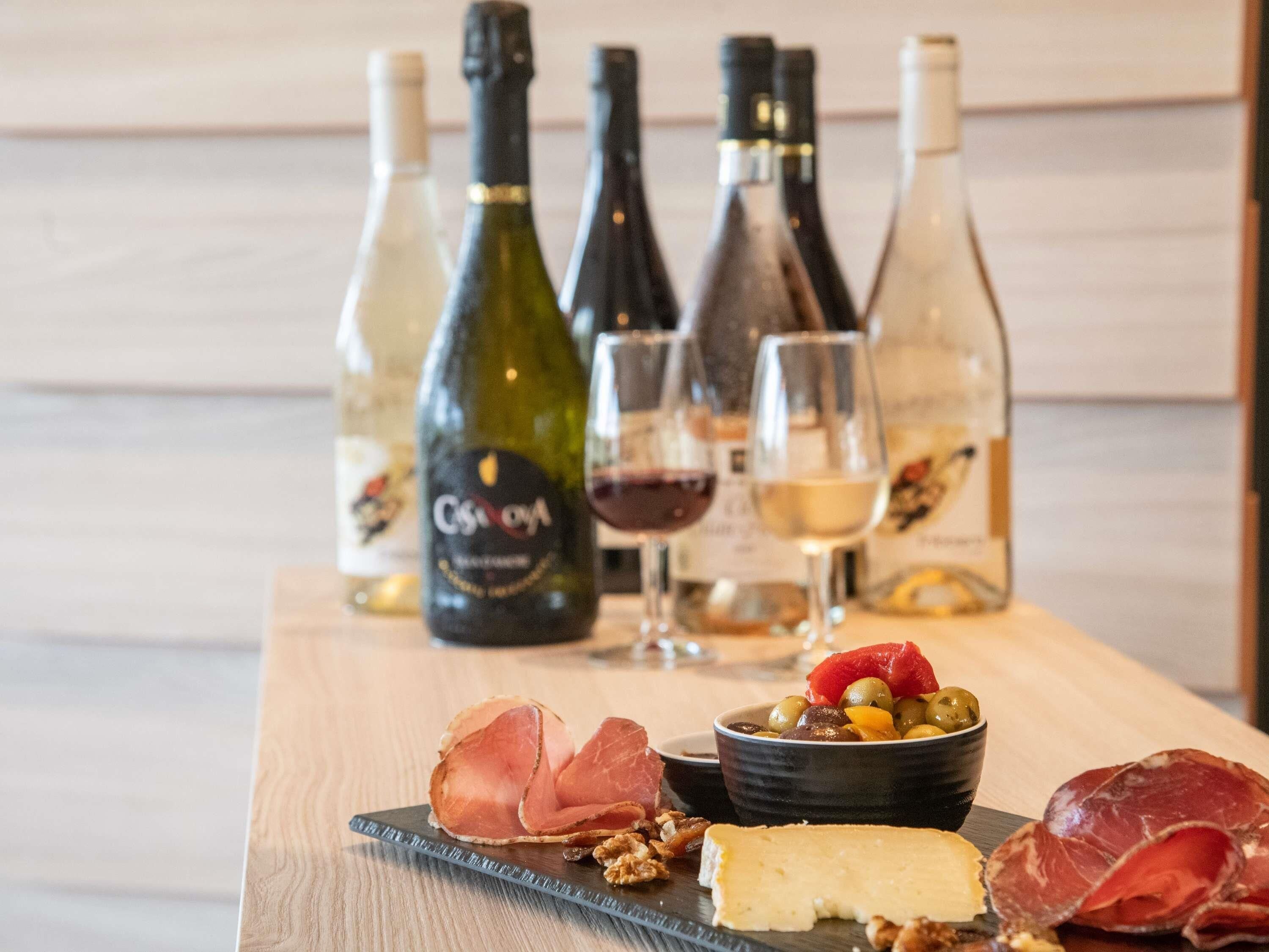 A wooden table with a selection of cheeses, cured meats, olives, and nuts, accompanied by several wine bottles and glasses.