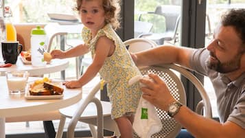 A dining area with a table set for two, featuring a meal, drinks, and a child interacting with a toy.