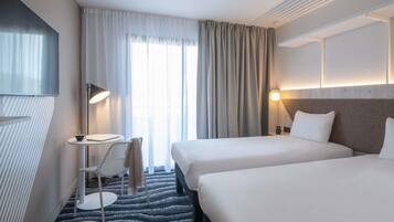 Habitación de hotel con dos camas, un escritorio, una silla, un televisor y una ventana con cortinas.