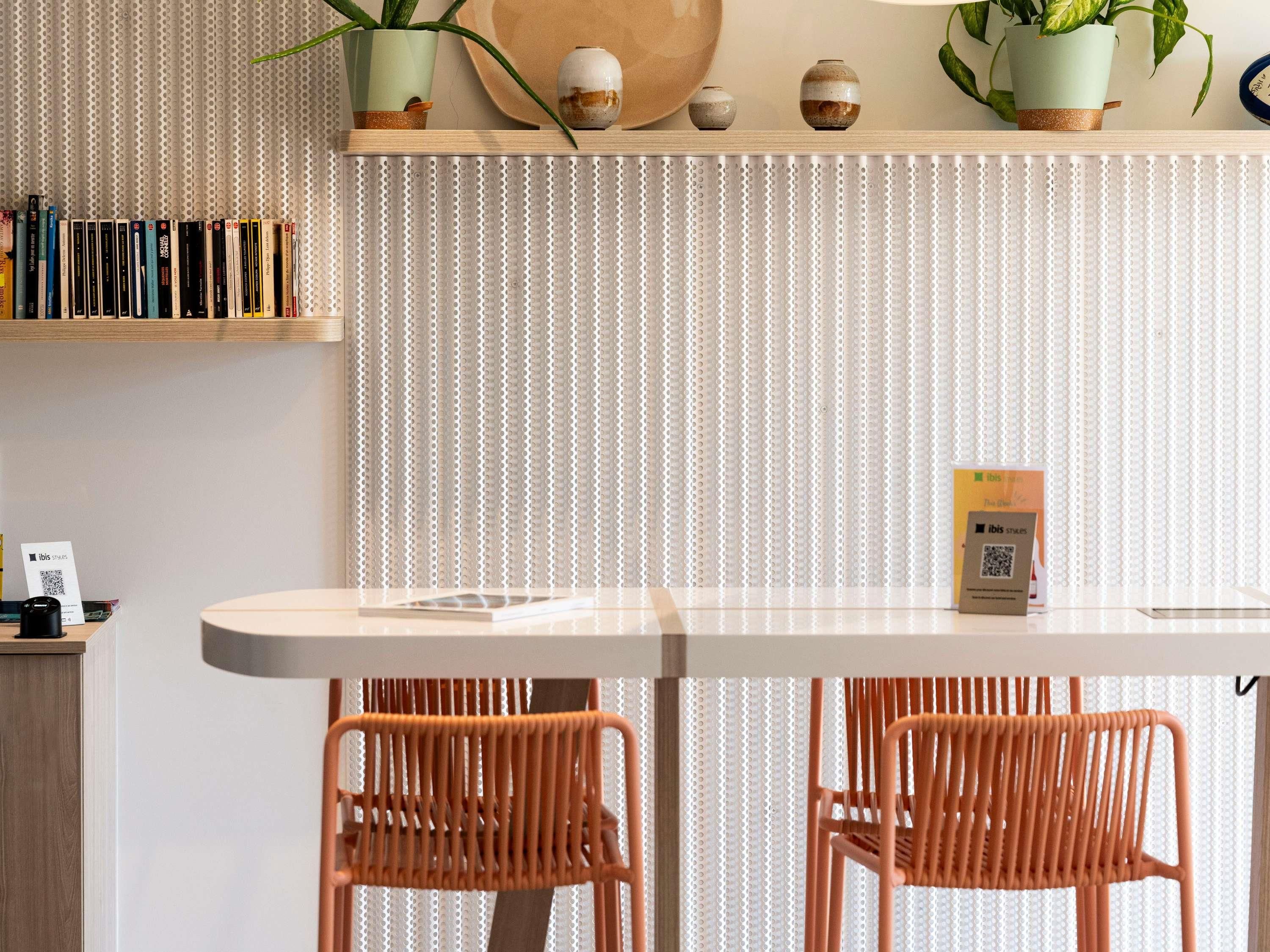 A modern dining area with a white table, two orange chairs, a patterned wall, and decorative items on shelves.