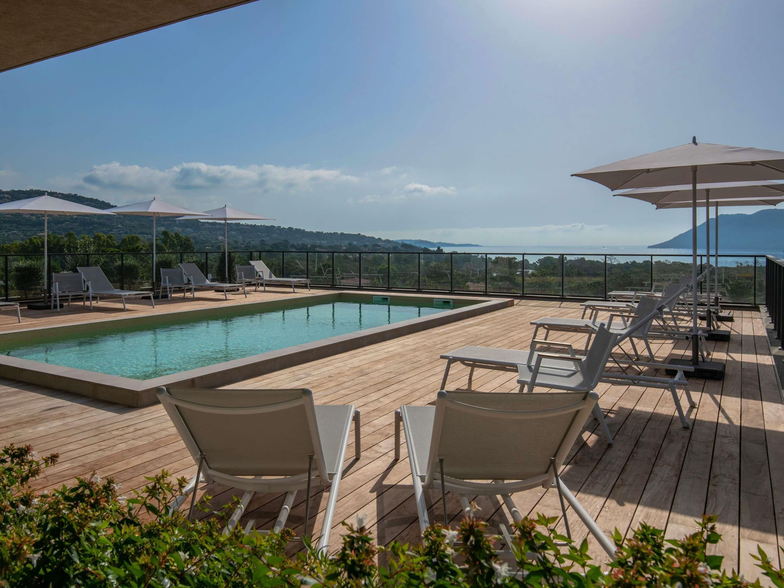 Zona de piscina en la azotea con sillas de descanso y sombrillas, con vistas a un paisaje montañoso.
