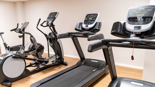 A row of stationary exercise machines, including treadmills and elliptical trainers, in a room with wooden flooring. - Ibis Styles Porto Vecchio (Porto-Vecchio)