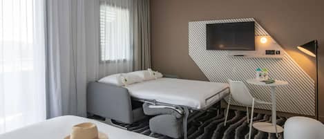 Una habitación de hotel con una cama, un escritorio, un televisor y un ventanal con cortinas.