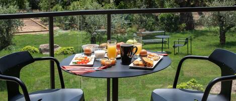 A balcony with a table set for breakfast, two chairs, and a view of a garden.