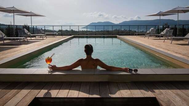En person som kopplar av i en pool med utsikt över berg och hav.