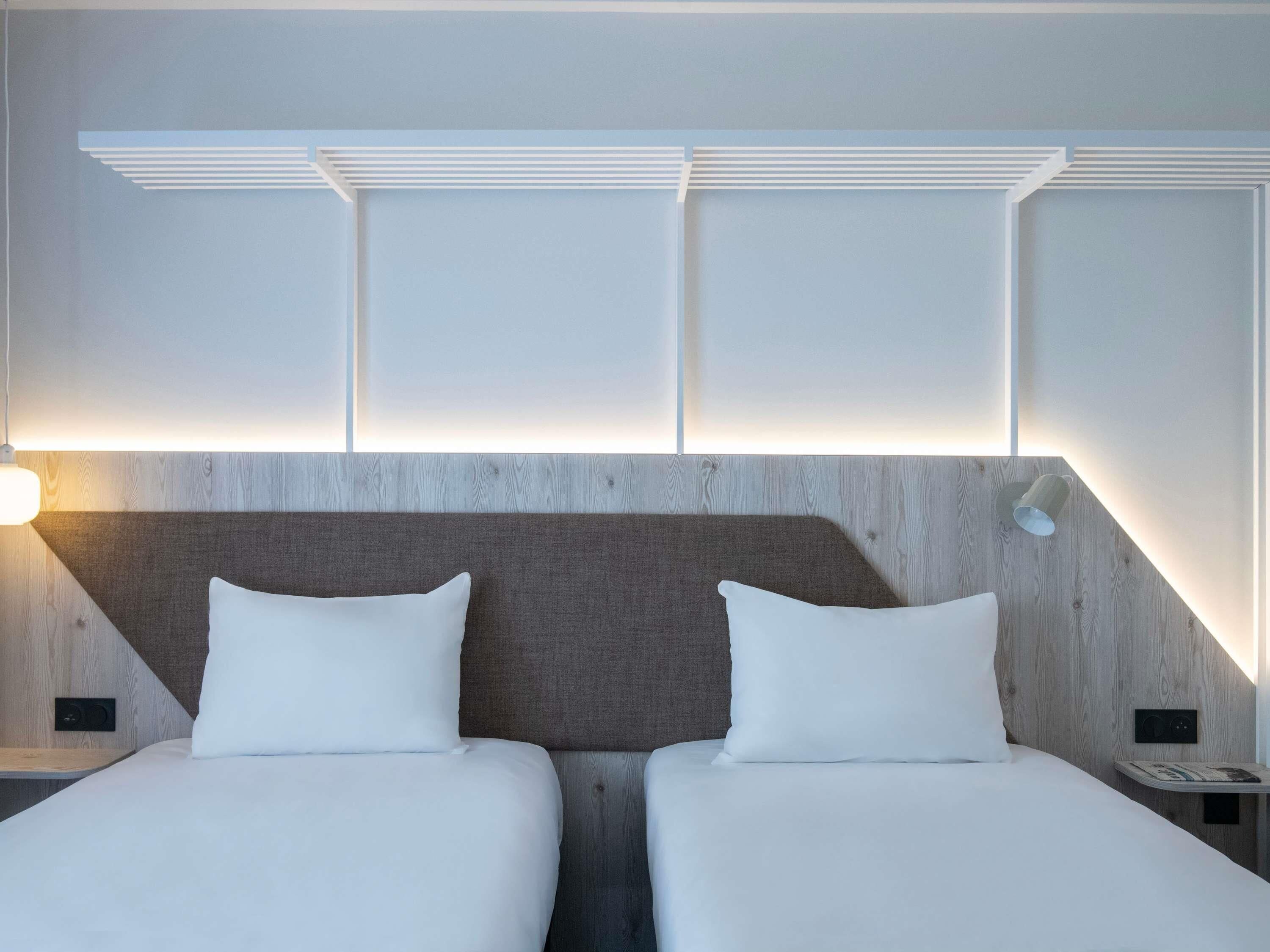 A hotel room with two beds, a wooden headboard, and a wall-mounted light fixture.