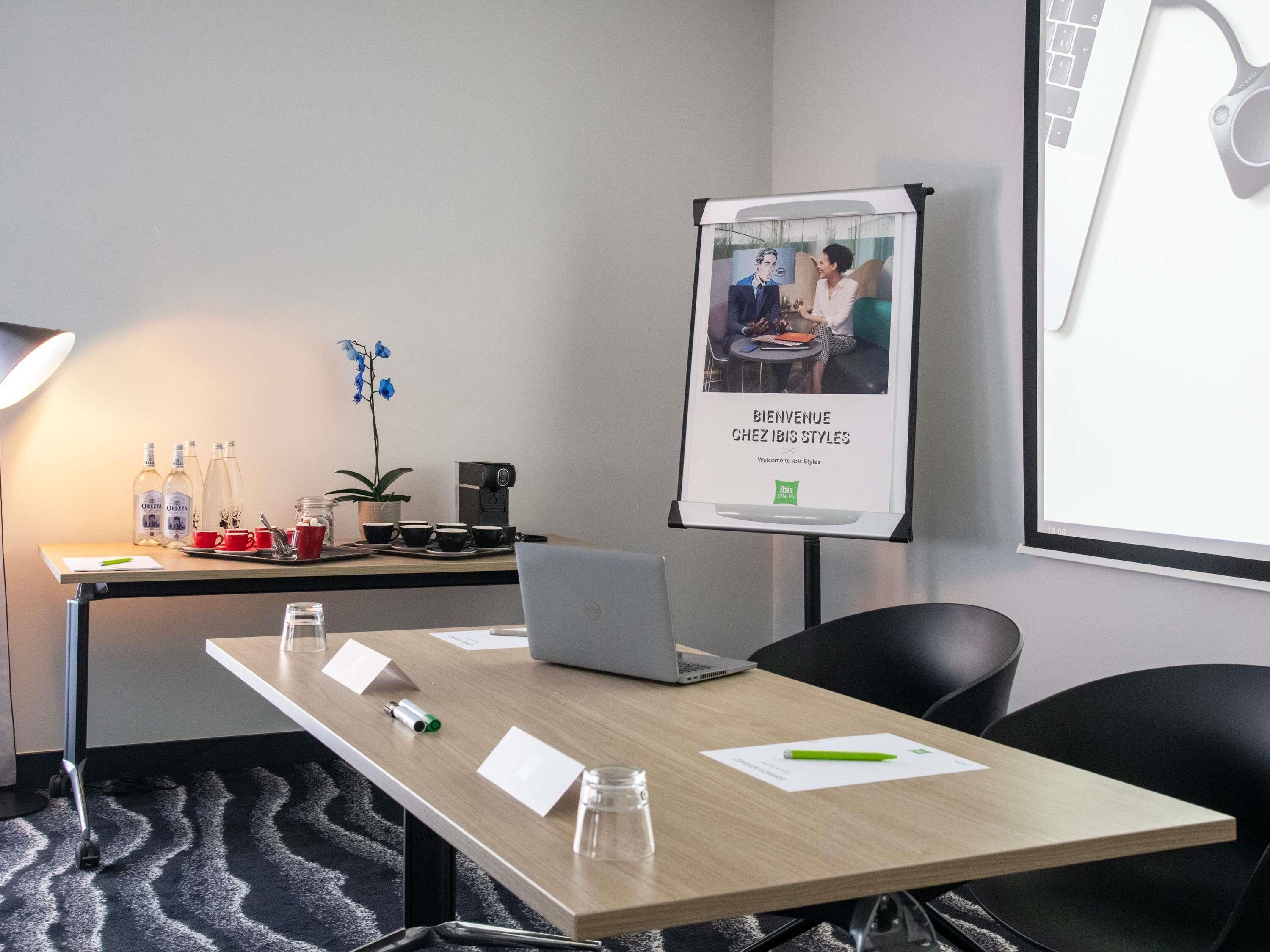 A conference room with a laptop, a coffee machine, and a banner.