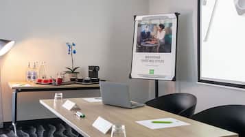 Un salón de conferencias con una computadora portátil, una máquina de café y un cartel.
