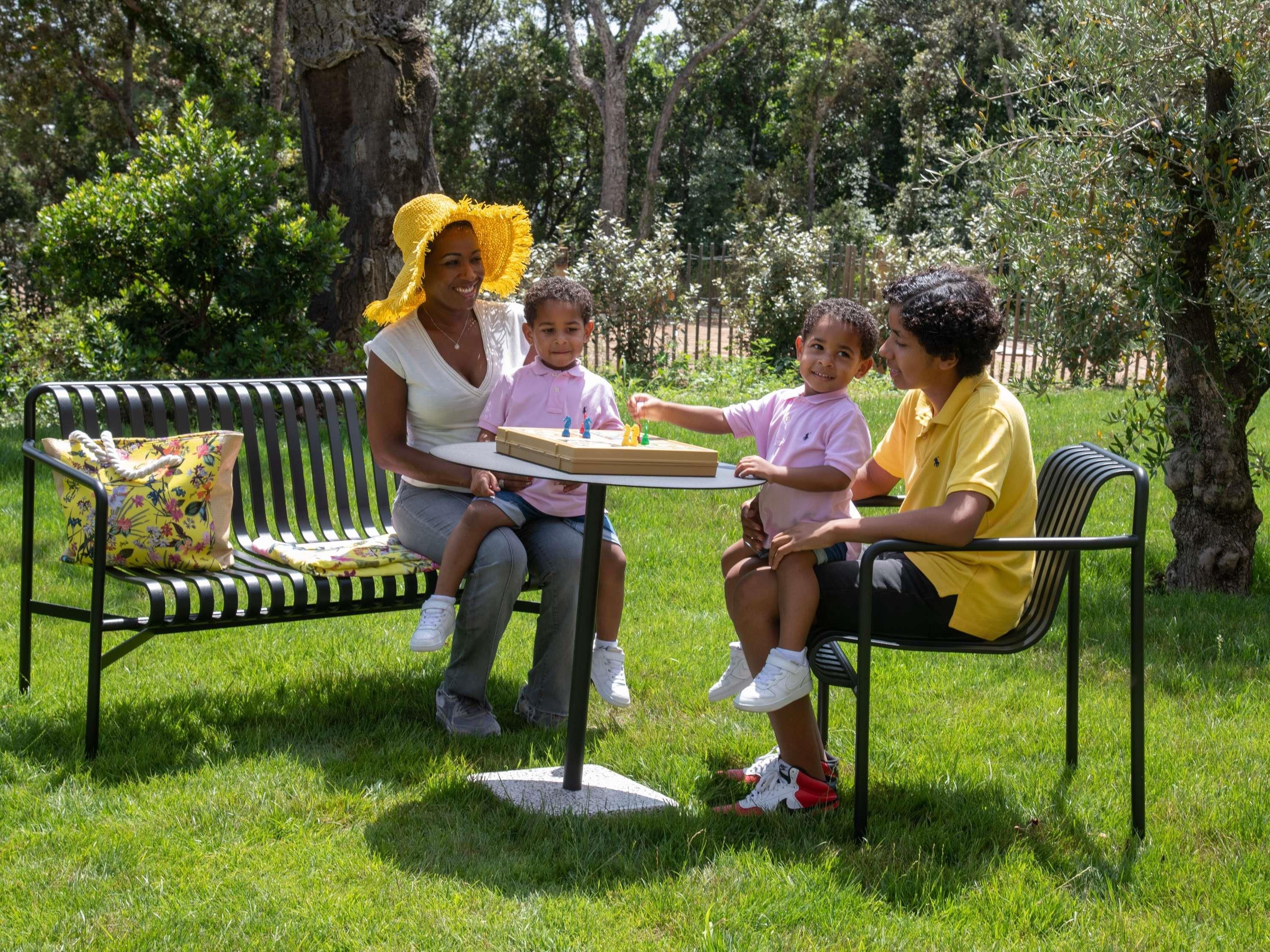 A group of people sitting on a bench in a park with a table in front of them.