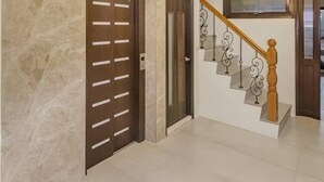 A spacious hallway with a marble wall, a wooden door, and a staircase with a wooden handrail and metal balusters. - Spring Rain Hostel (Meishan)
