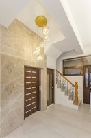 Un pasillo amplio con pared de mármol, una puerta de madera y una escalera con barandilla de madera y barandillas de metal.