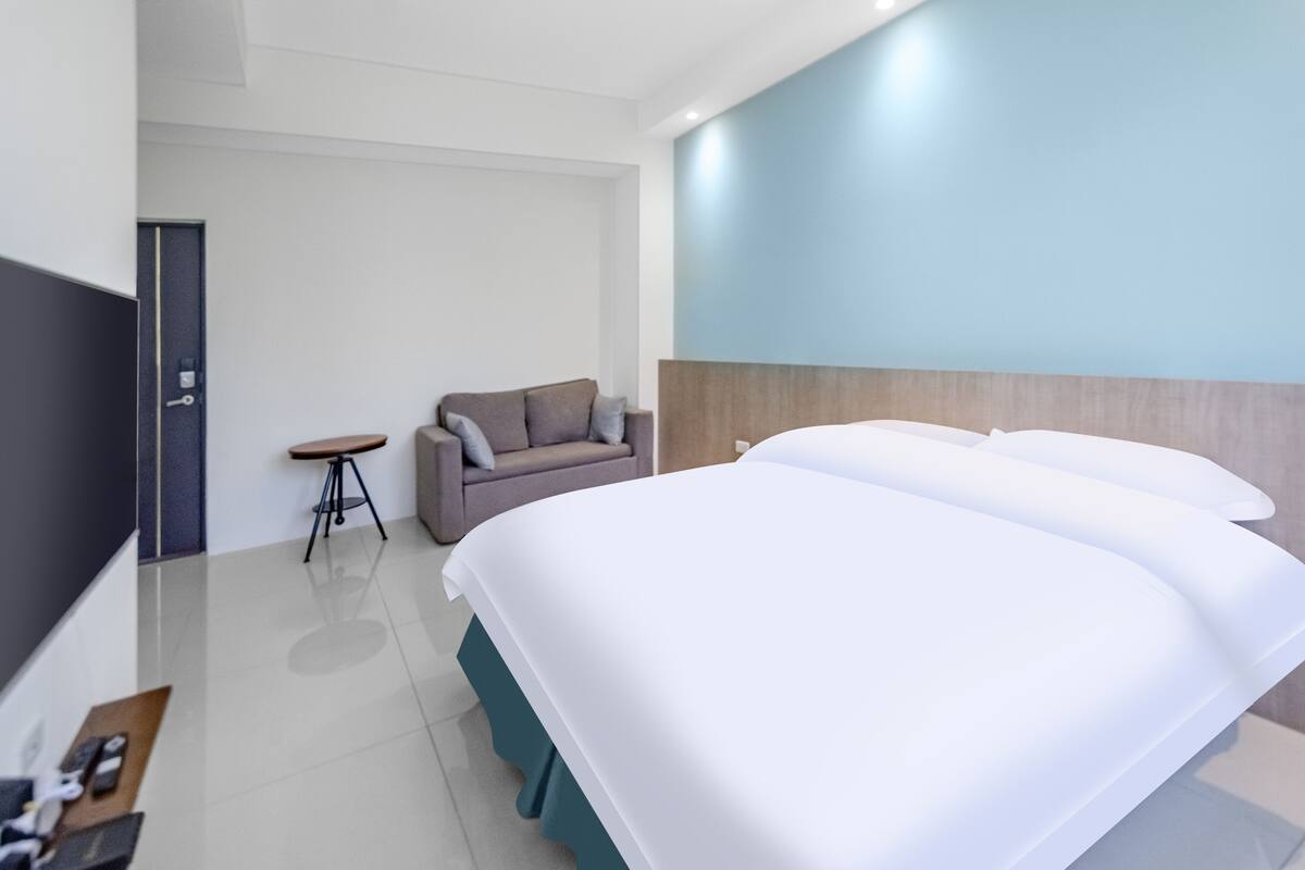 A modern hotel room with a large bed, a small sofa, a side table, and a TV.