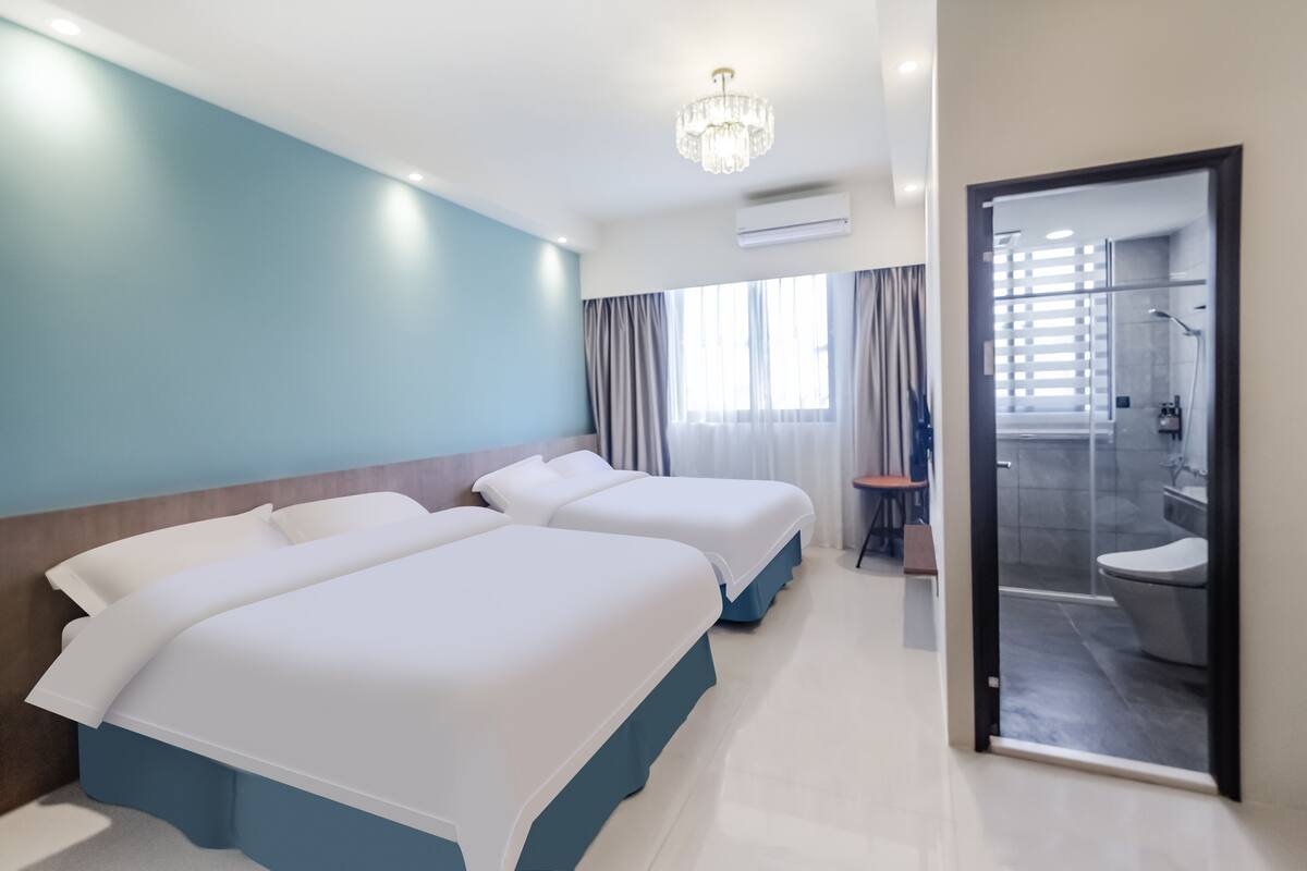 A hotel room with two beds, a chandelier, a shower area, and a view of the outside.