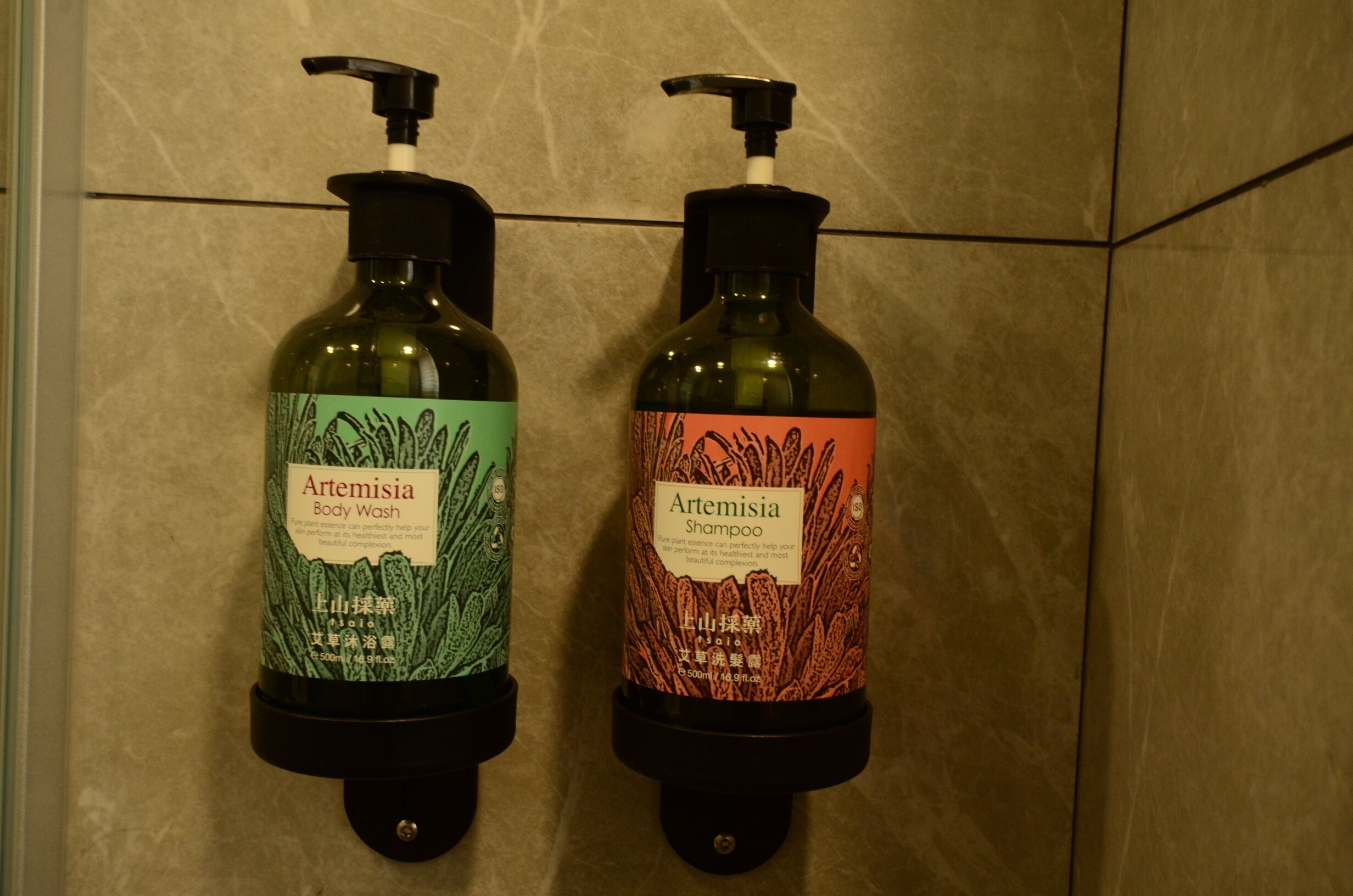 Two bottles of Artemisia body wash and shampoo on a tiled wall.