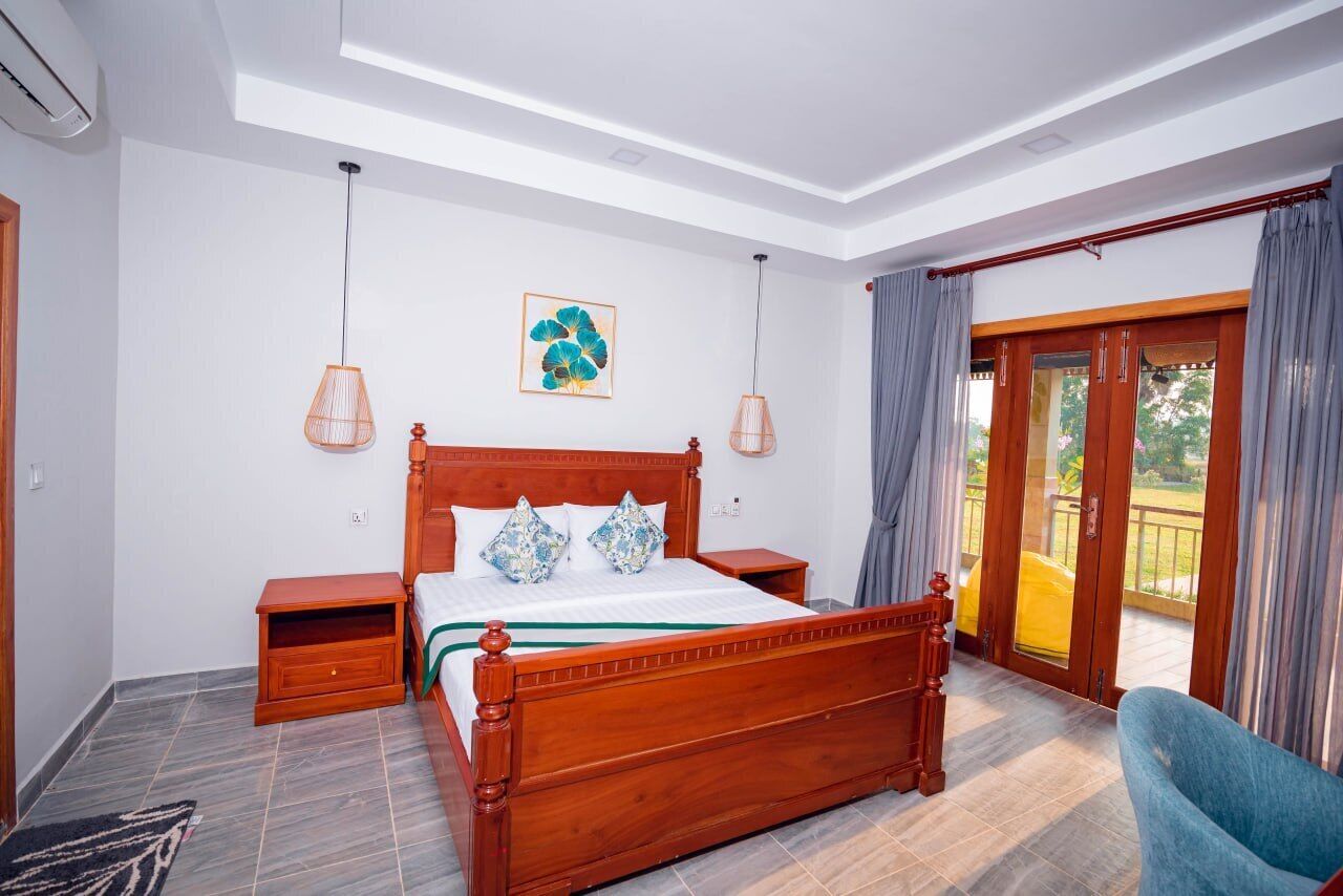 Una camera da letto con un letto in legno, due comodini, un tavolino e una grande finestra con tende, e vista sull'esterno.