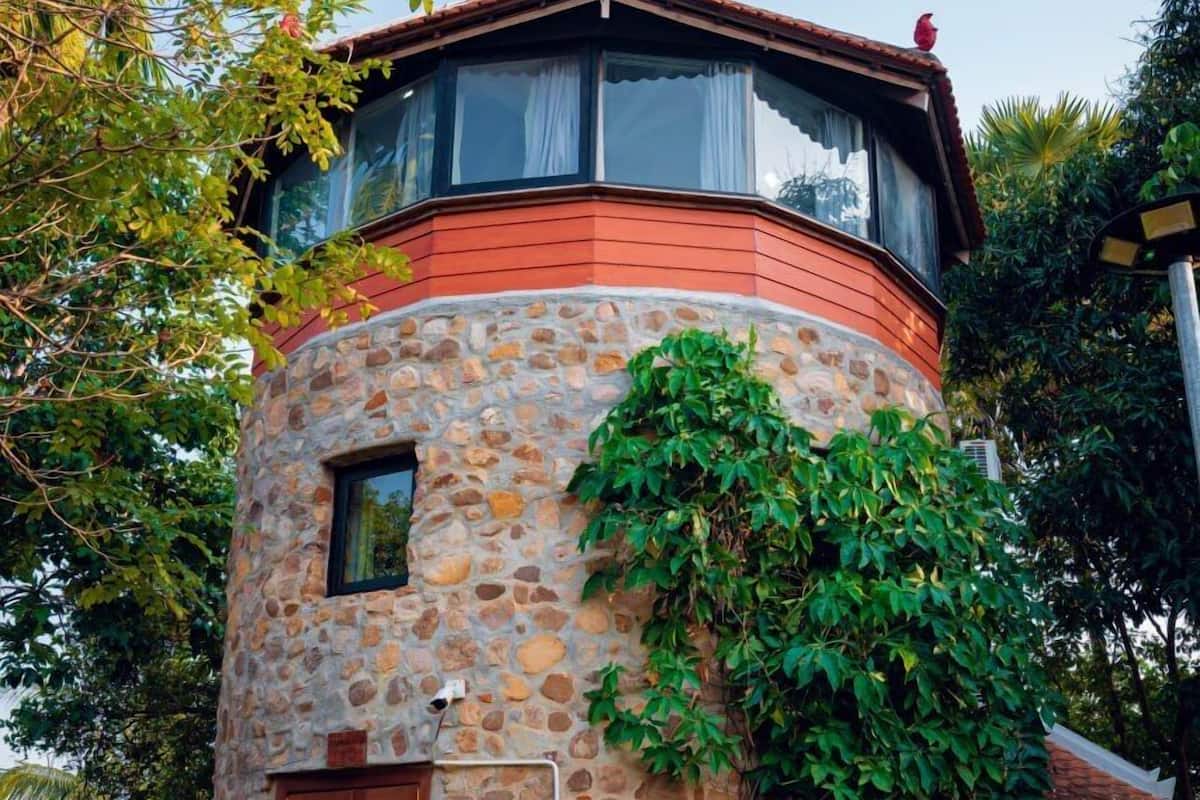 Uma torre de pedra com porta e janela de madeira, cercada por vegetação.