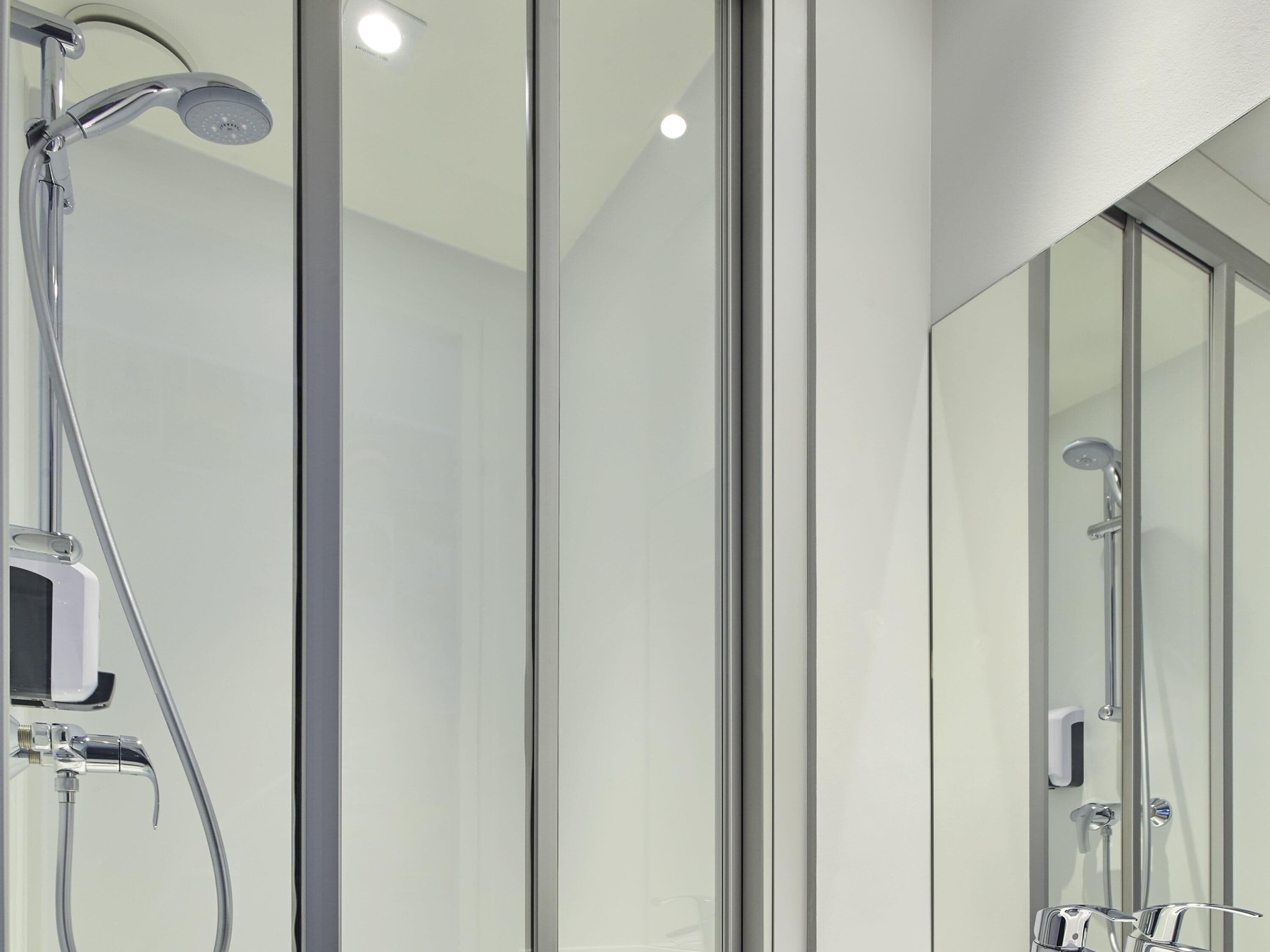 A modern bathroom with a glass shower enclosure, a handheld showerhead, and a wall-mounted faucet.