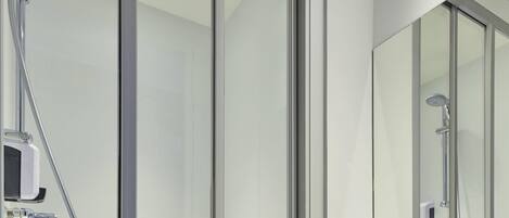 A modern bathroom with a glass shower enclosure, a handheld showerhead, and a wall-mounted faucet.