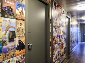 Un couloir aux murs ornés d’affiches de voyage, une porte et un plancher en bois.