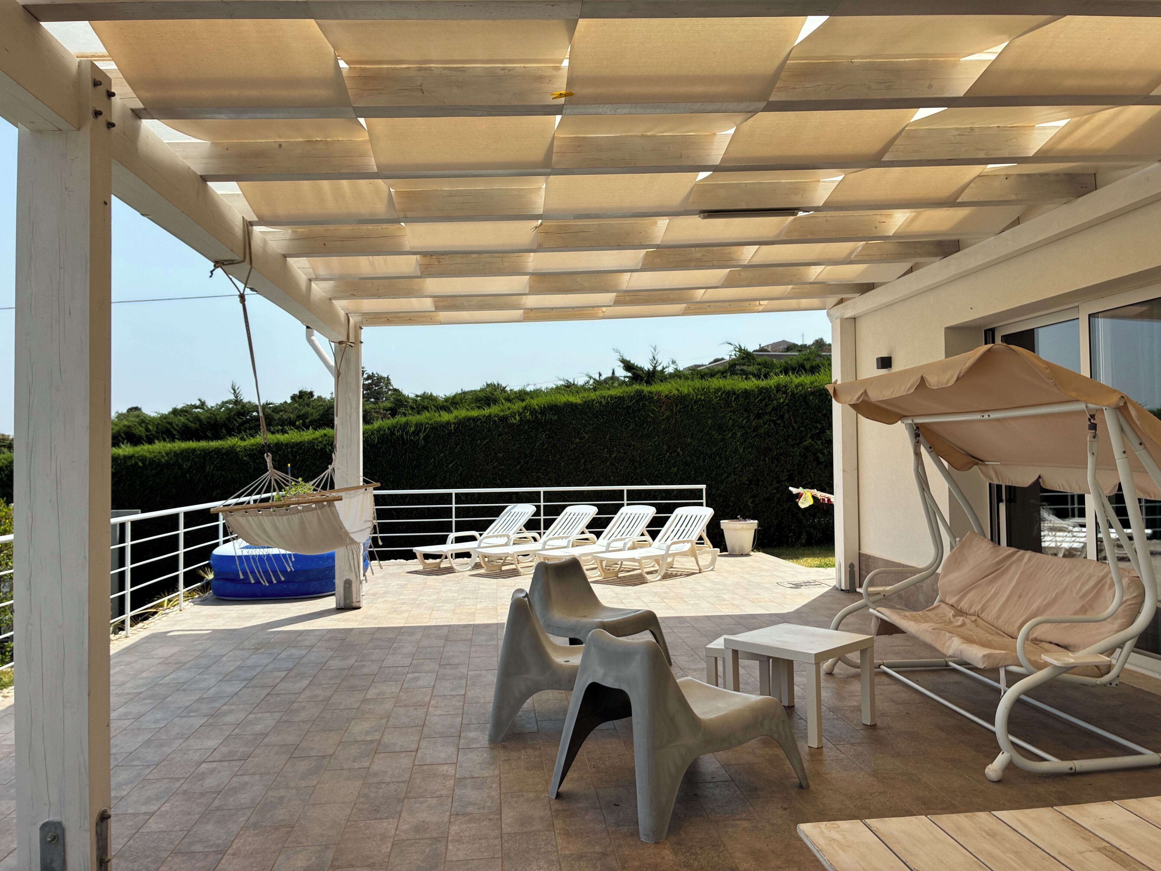 A covered outdoor seating area with lounge chairs and a swing chair, a small table, and a hanging chair.